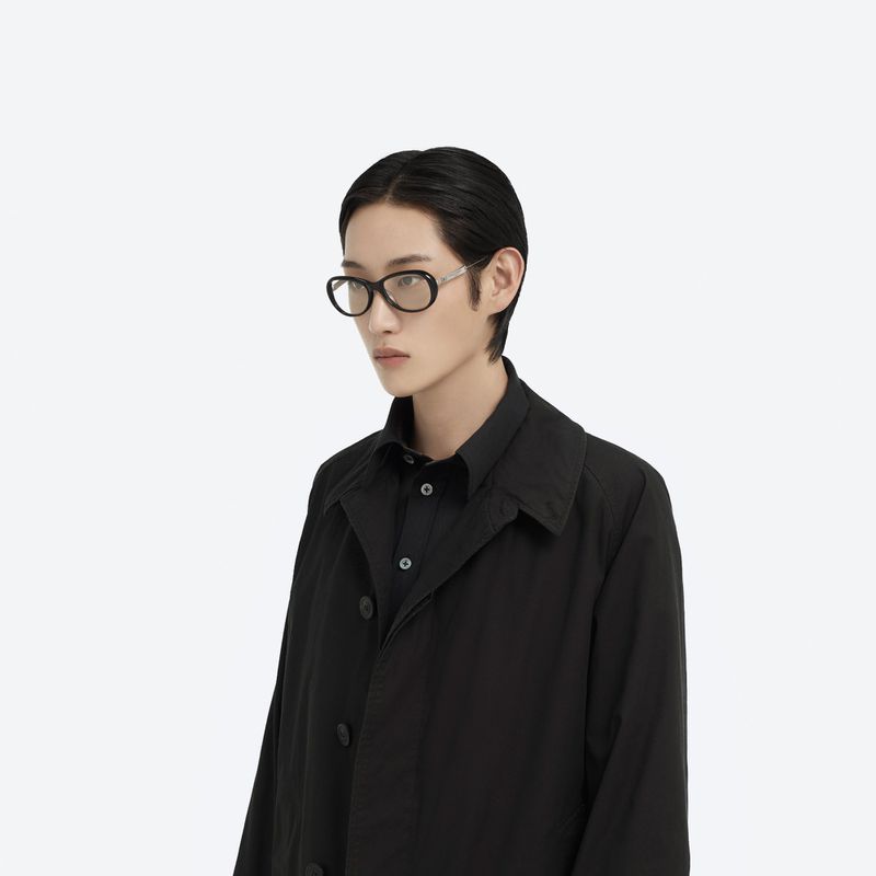 Model wearing black eyeglasses and a black shirt against a plain white background for Maison Margiela X Gentle Monster
