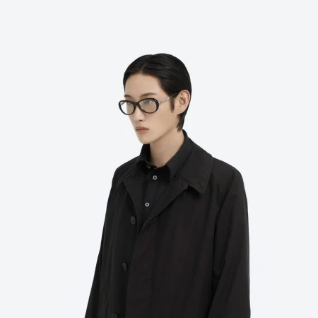 Model wearing black eyeglasses and a black shirt against a plain white background for Maison Margiela X Gentle Monster