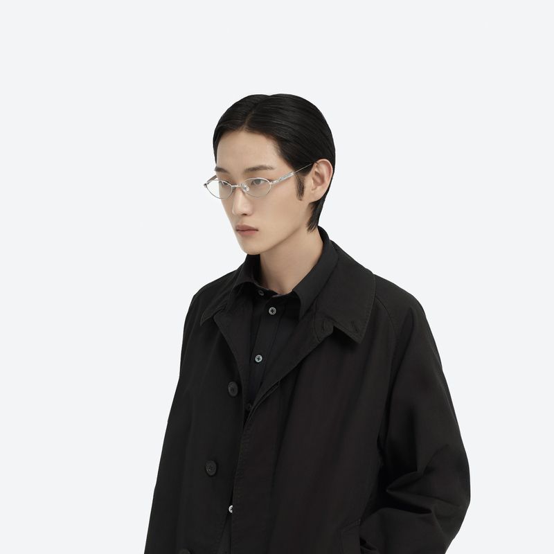 Studio shot of an East Asian adult male model with black hair wearing translucent geometric glasses, black collared shirt, and black coat.