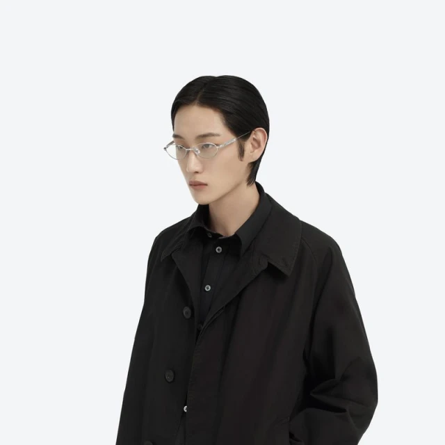 Studio shot of an East Asian adult male model with black hair wearing translucent geometric glasses, black collared shirt, and black coat.