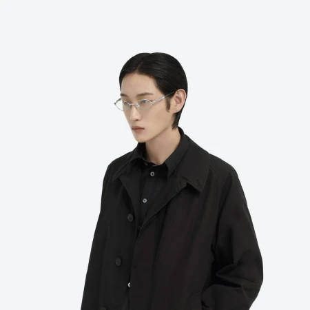 Studio shot of an East Asian adult male model with black hair wearing translucent geometric glasses, black collared shirt, and black coat.
