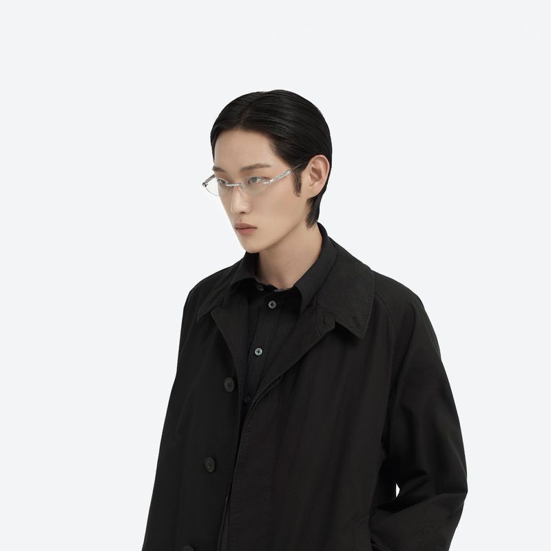 An Asian adult male model in a black trench coat and silver rim glasses poses in a neutral eye-level shot against a white background.