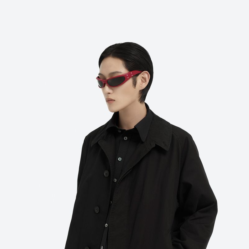 Model wearing red sunglasses and a black coat against a seamless white background for Maison Margiela X Gentle Monster