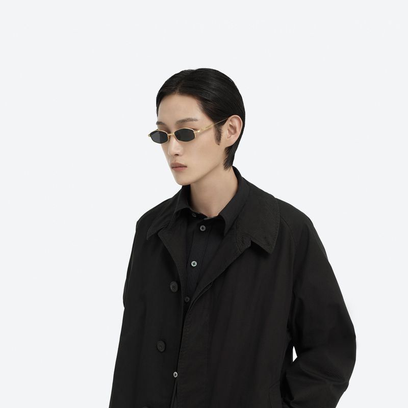 Asian male model posing in a black button-down shirt and coat wearing retro sunglasses against a bright white studio backdrop.