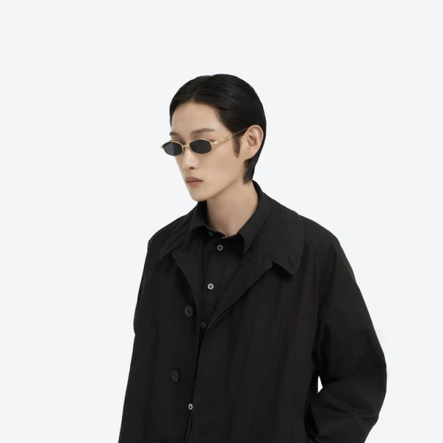 Asian male model posing in a black button-down shirt and coat wearing retro sunglasses against a bright white studio backdrop.