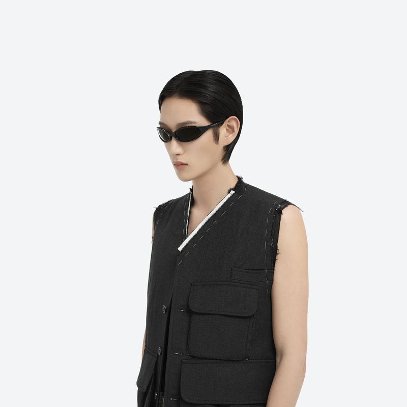 Model wearing black sunglasses and a dark grey utility vest against a white seamless background