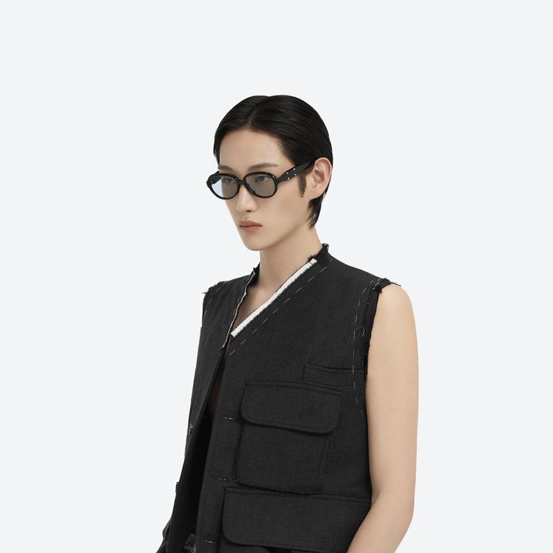 Adult human wears a utility vest and tinted eyeglasses in a studio portrait against a white backdrop. Fashion, beauty, and style.