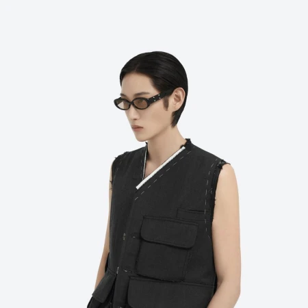 Model wearing dark sunglasses and a black utility vest against a plain white background for Maison Margiela X Gentle Monster.