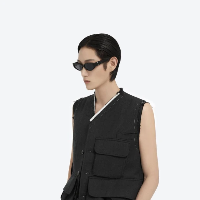 Adult male poses in a black vest and sunglasses against a white background, showcasing fashion and editorial style with a focus on modern aesthetics.