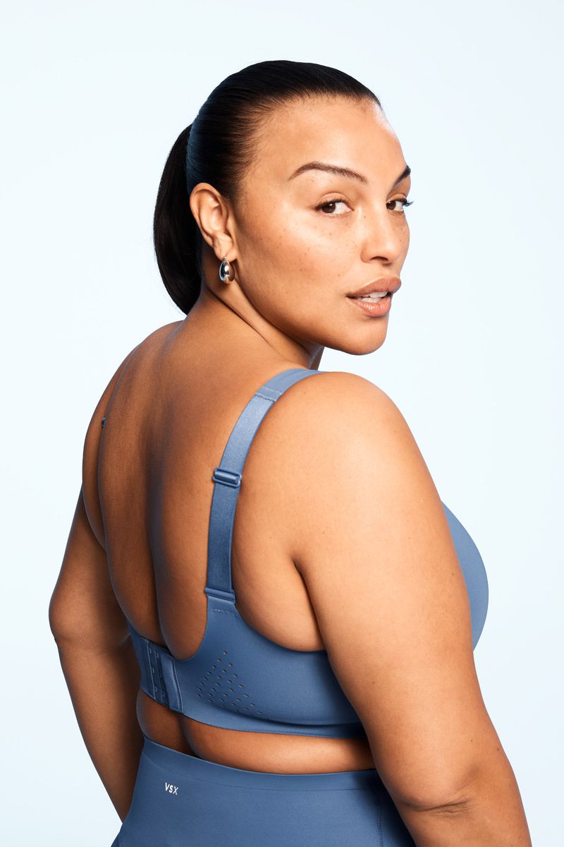 A woman with her hair pulled back in a ponytail is facing away from the camera, but looks over her shoulder toward it. She is wearing a blue sports bra.