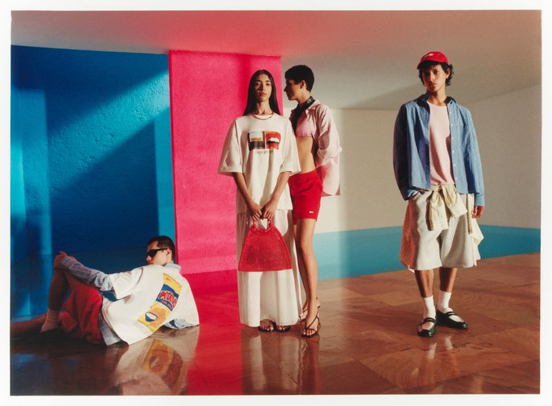 Four fashion models in brightly coloured studio setting; two women in white outfits, and two men wearing casual summer apparel.