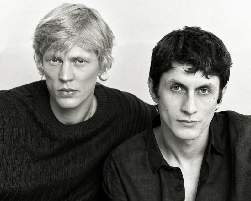 Monochrome portrait of two male models with dark clothing posing against a plain background for Massimo Dutti.