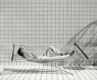 A man lying relaxed in a white string hammock against a tiled wall in a campaign image for Massimo Dutti.