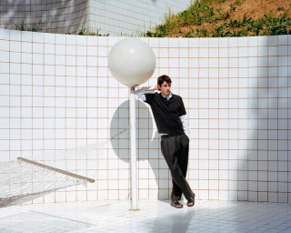 Model leaning against a tall round lamp post before a white tiled wall in the Massimo Dutti Quiet Move campaign.