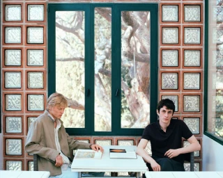 Two male models seated at a table indoors against a wall of square glass blocks and large windows for Massimo Dutti.
