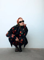 Model in black floral print jacket and matching trousers crouching against a white background.