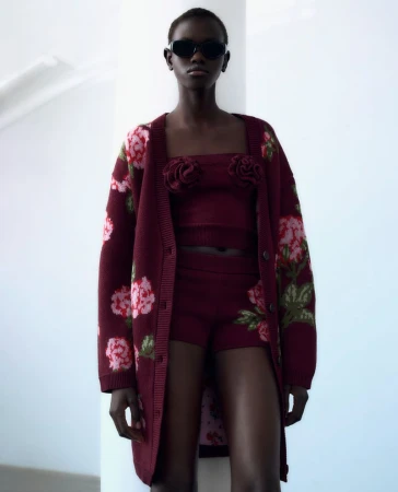 Model wearing dark sunglasses, burgundy floral cardigan, matching top, and shorts against a bright white background.