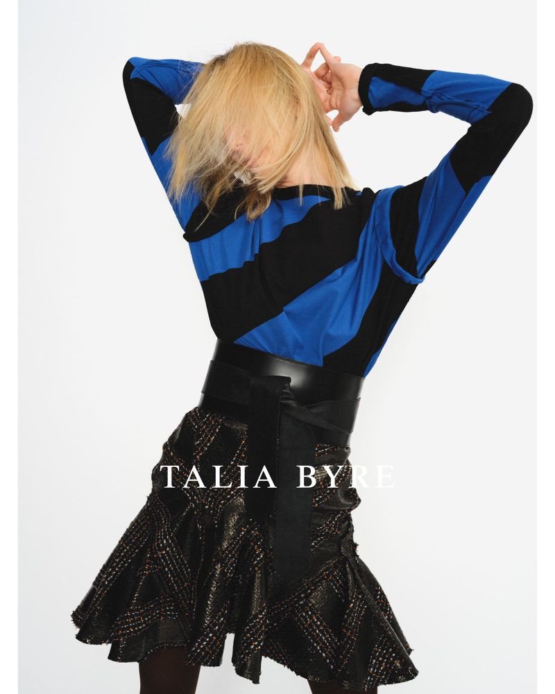 Model with blonde hair obscuring face wearing blue and black striped long-sleeve top and flared skirt against a white background