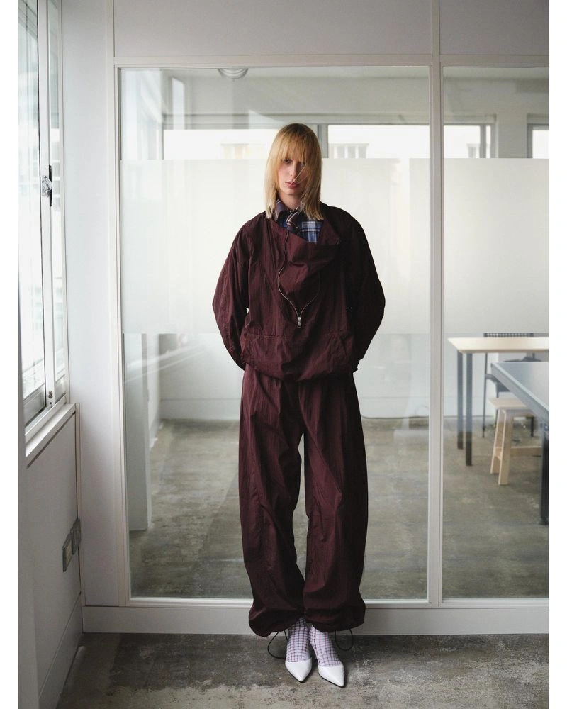 Model wearing a plaid wrap top, pleated skirt, purple tights, and a yellow beanie in an interior office setting
