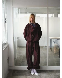 Model wearing a plaid wrap top, pleated skirt, purple tights, and a yellow beanie in an interior office setting