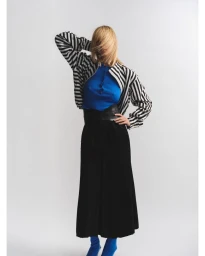 Model with blonde hair obscuring face wearing a striped jacket, blue top, and black skirt against white background