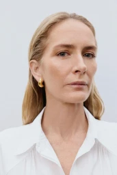 Close-up portrait of Georgina Grenville wearing a white shirt and gold earrings against a plain white background