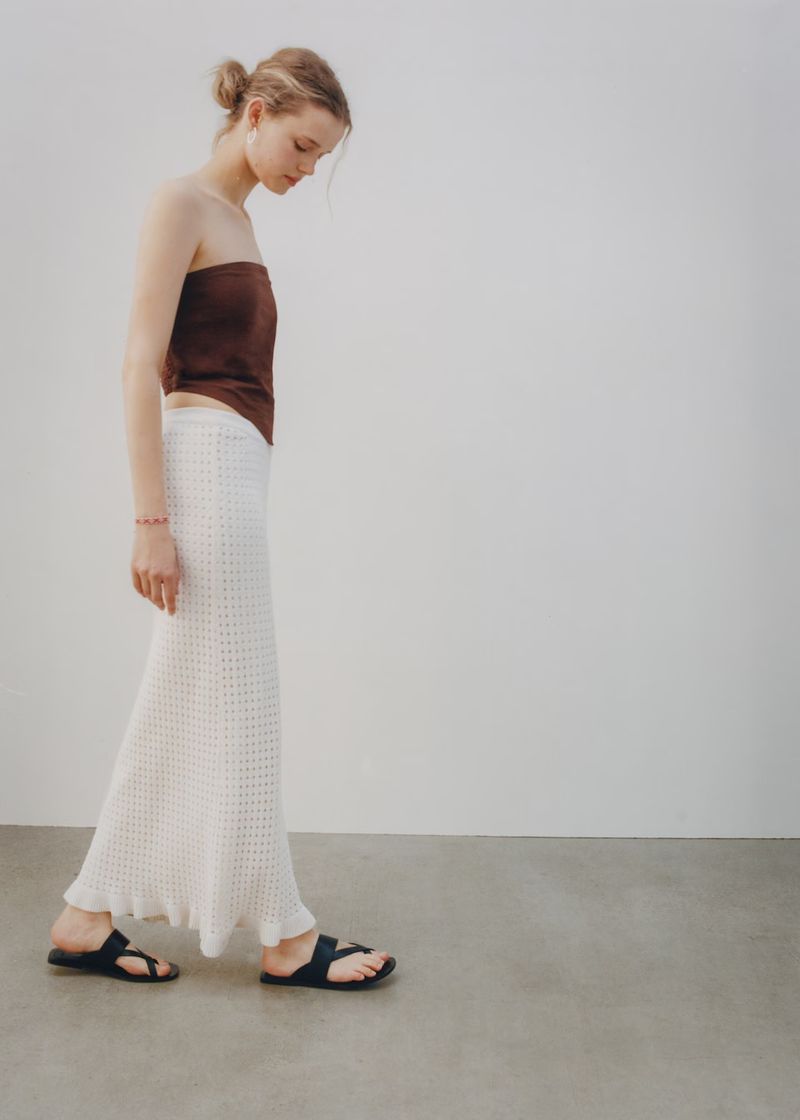 Model wearing a brown strapless top and white knit maxi skirt against a seamless neutral background