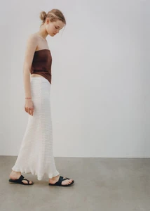 Model wearing a brown strapless top and white knit maxi skirt against a seamless neutral background