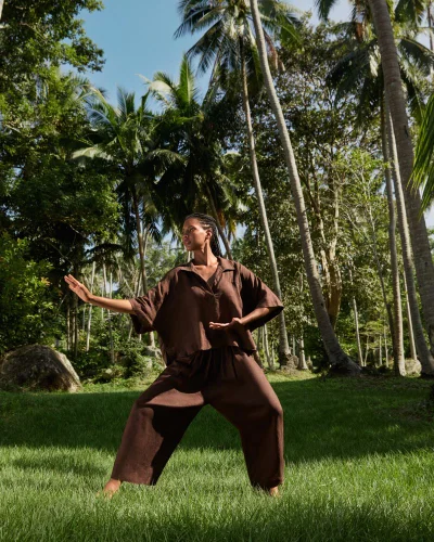 Model in brown linen outfit posing in a tropical clearing surrounded by tall palm trees