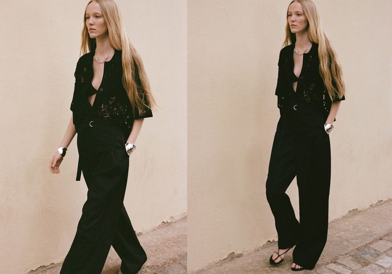 A fashionable adult female with long blond hair walks in black top and trousers against a plain background with neutral lighting.