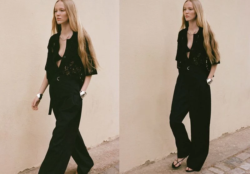 A fashionable adult female with long blond hair walks in black top and trousers against a plain background with neutral lighting.