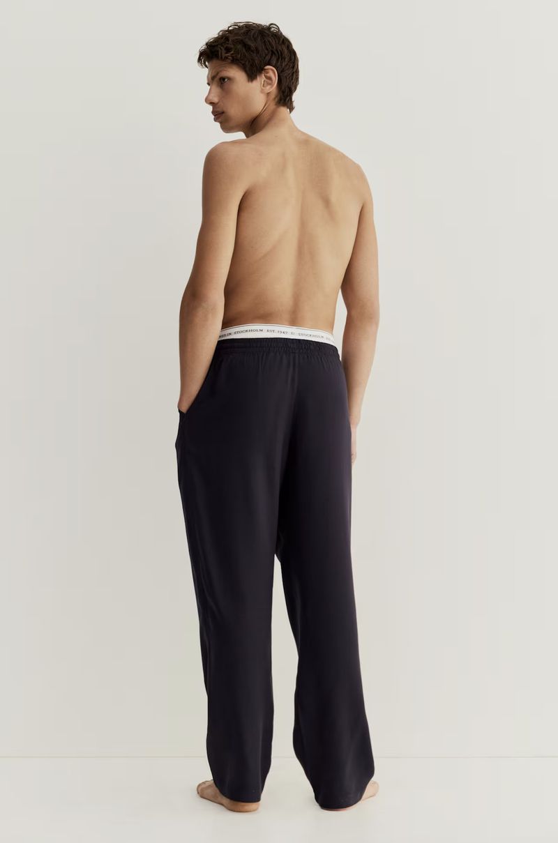 Adult male wearing dark lounge pants stands in a neutral, indoor studio setting, showcasing a relaxed and comfortable style.