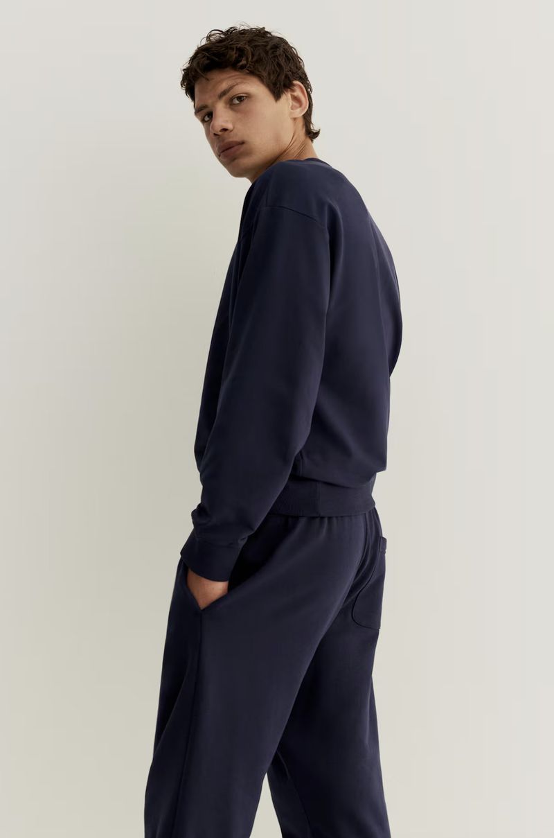 Male model wearing a navy blue sweatshirt and matching sweatpants against a plain light background