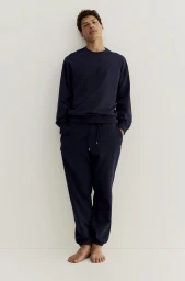 Model wearing dark blue sweatshirt and matching sweatpants standing against white seamless background