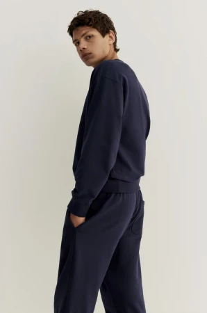 Male model wearing a navy blue sweatshirt and matching sweatpants against a plain light background