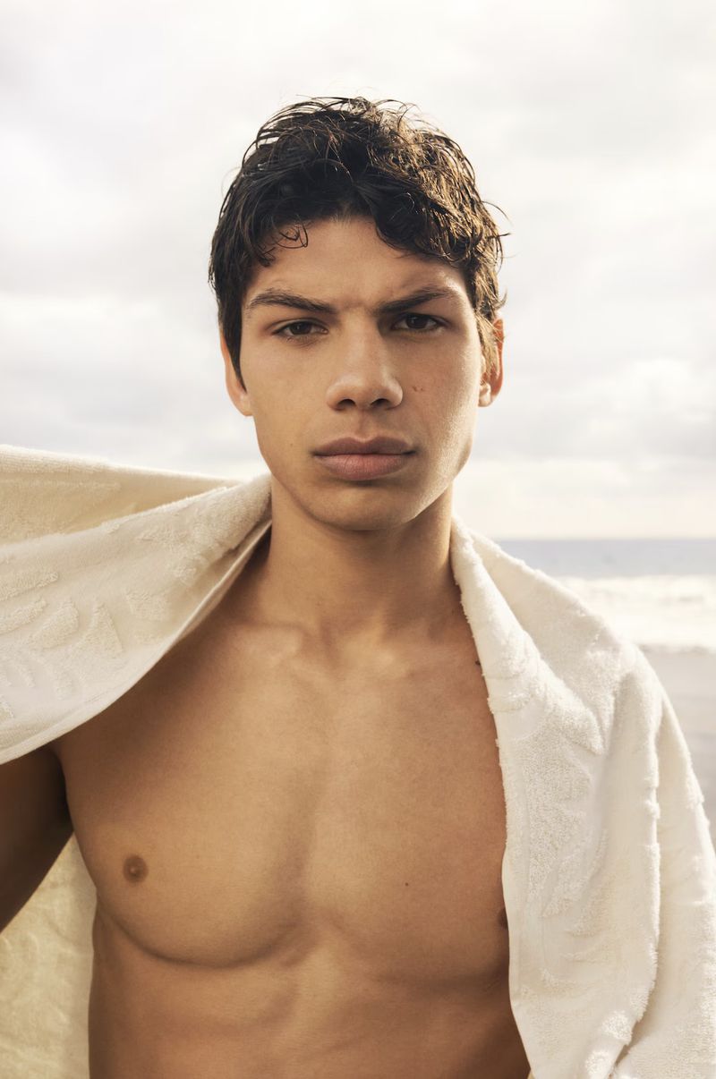 Portrait of a young man with a towel around his shoulders against a blurred background of a beach and sky.