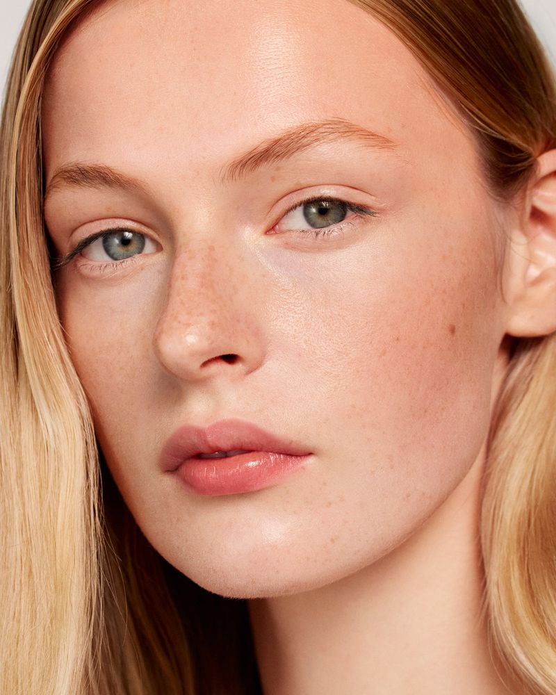 Close-up portrait of a fair-skinned woman with blonde hair and freckles, focusing on beauty and skincare with a clean, minimalist aesthetic.