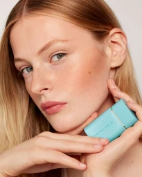 Close-up beauty portrait of a woman holding a turquoise Westman Atelier cosmetic product near her cheek
