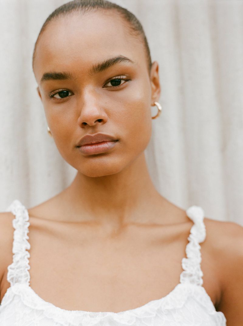 Close-up portrait of a model with short hair wearing a white top against a neutral textured background