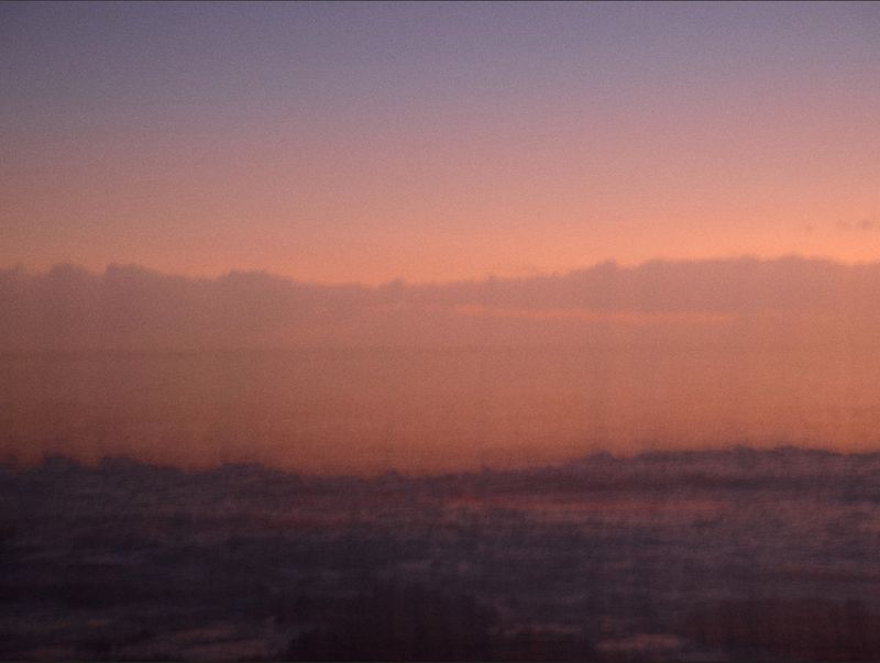 Sunrise or sunset sky with purple and orange hues over soft, low clouds. The scene has a hazy, atmospheric quality.