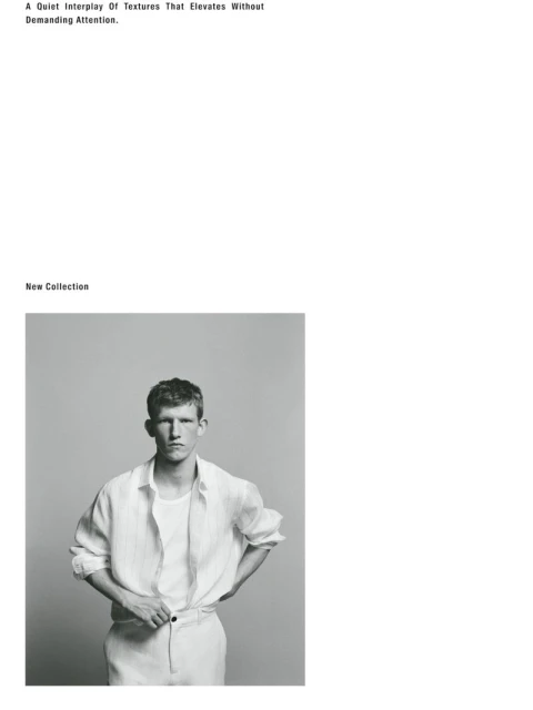 A black-and-white portrait of a young man wearing a linen shirt, standing against a gray background in a fashion-editorial style.