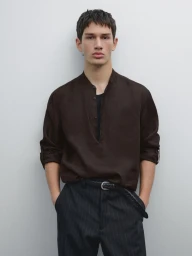 Model in dark brown shirt and pinstripe trousers against a plain white studio background