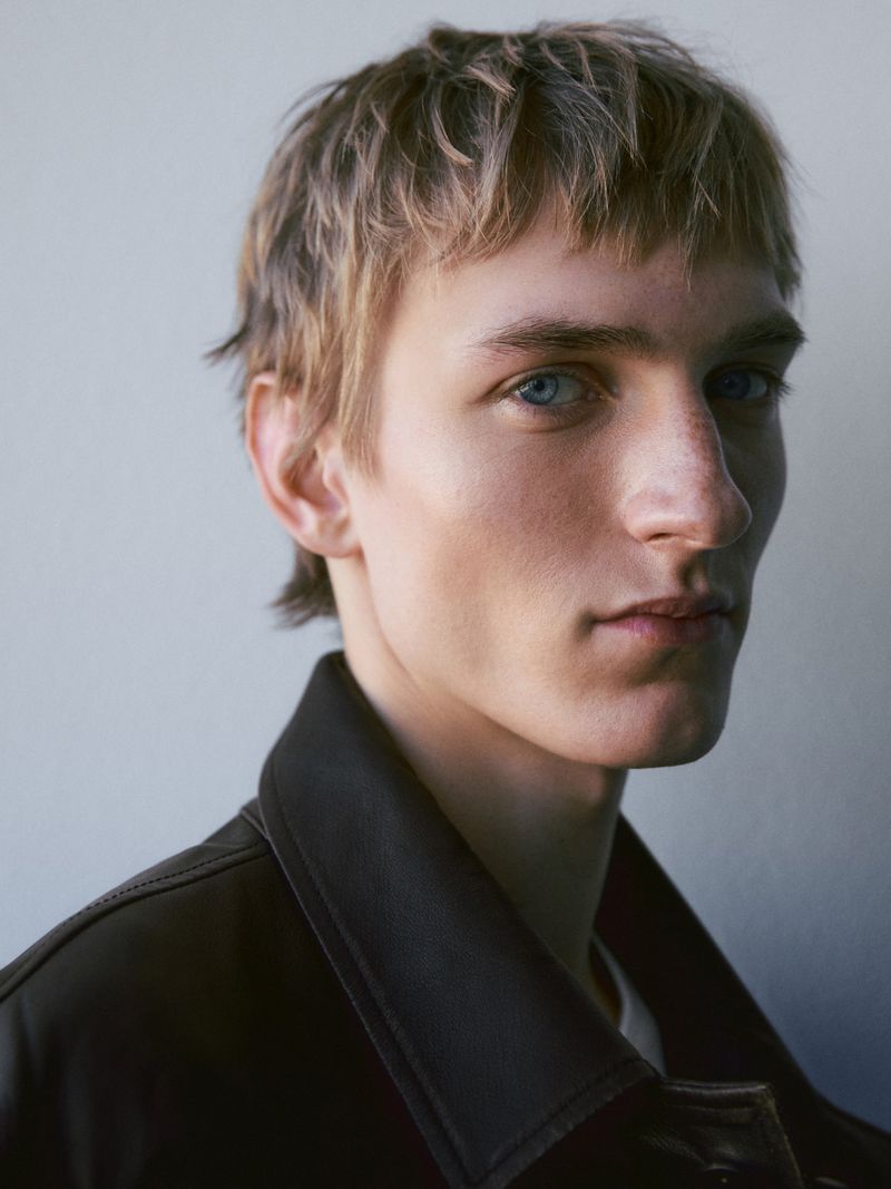Close-up portrait of a male model wearing a dark collar against a plain neutral background