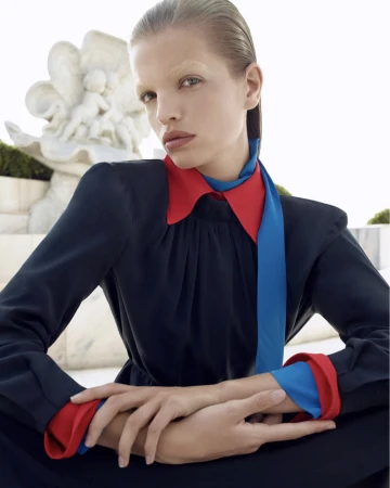 Portrait of a fashion model in a navy dress with red and blue accents, posing outdoors near a white sculpture on a bright day.