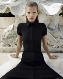 Model Daphne Groeneveld wearing a black collared dress seated in front of ornate stone architecture for Scanlan Theodore Winter 23.