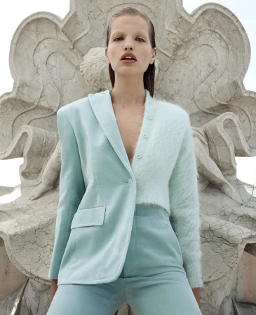 Woman posing in a two-tone jacket and pants against a stone sculpture. Fashion shot with a blend of textures and neutral tones.