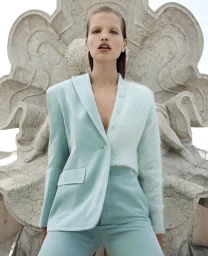 Model Daphne Groeneveld wearing a light blue blazer and pants posed against an ornate stone fountain sculpture for Scanlan Theodore