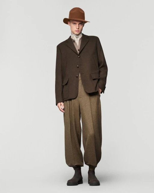 Full-length studio shot of an adult male wearing a brown hat, jacket, and pants. The man poses against a neutral grey background.