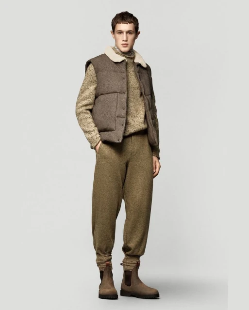A young man in a puffer vest, sweater, and sweatpants poses against a neutral background, showcasing a blend of casual and comfortable fashion.