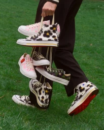 Person holding multiple pairs of patterned Converse sneakers by their laces outdoors over grass